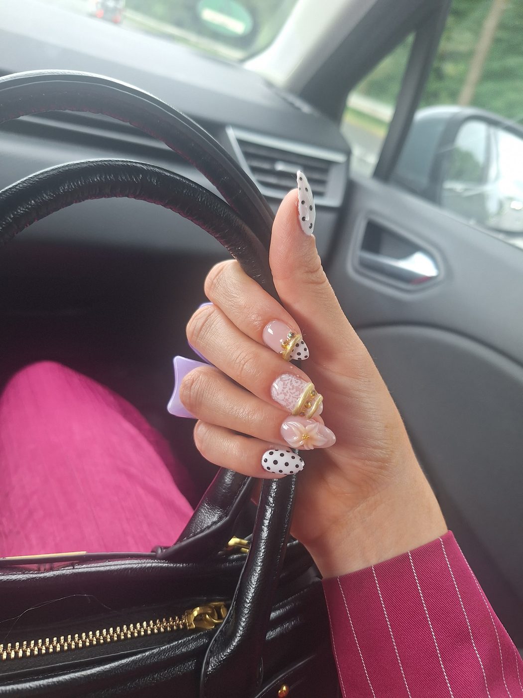 Hand met gestipte nagels en goudkleurige accenten aan een tas in de auto