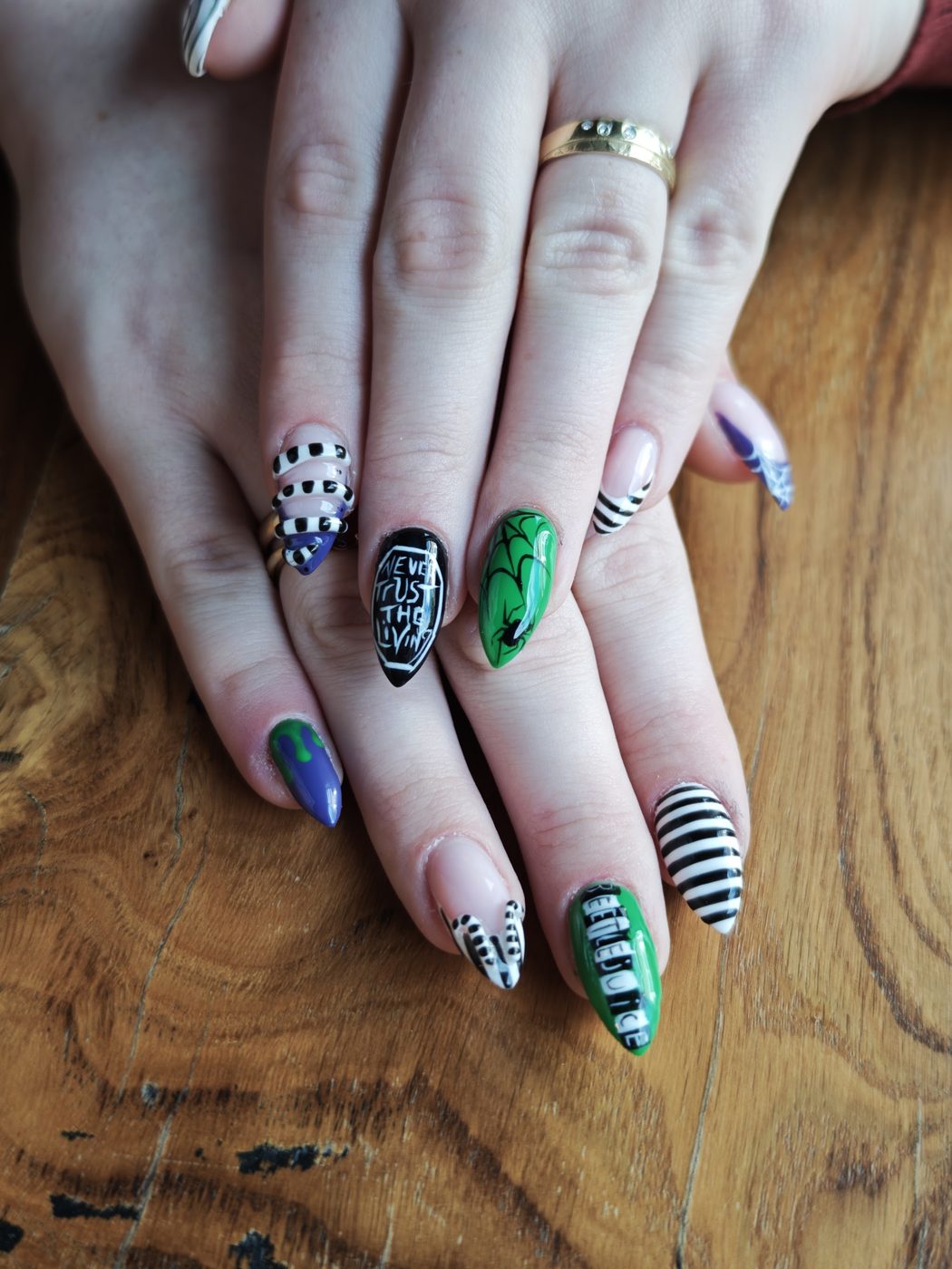 Twee handen met zwart-wit gestreepte en groene nail art op een houten tafel