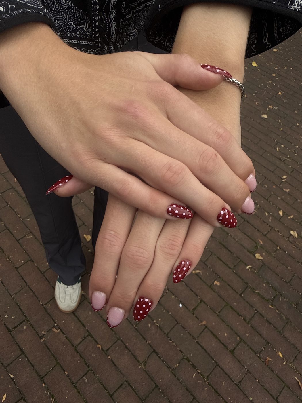 Handen met rode nagels met witte stippen boven straatklinkers